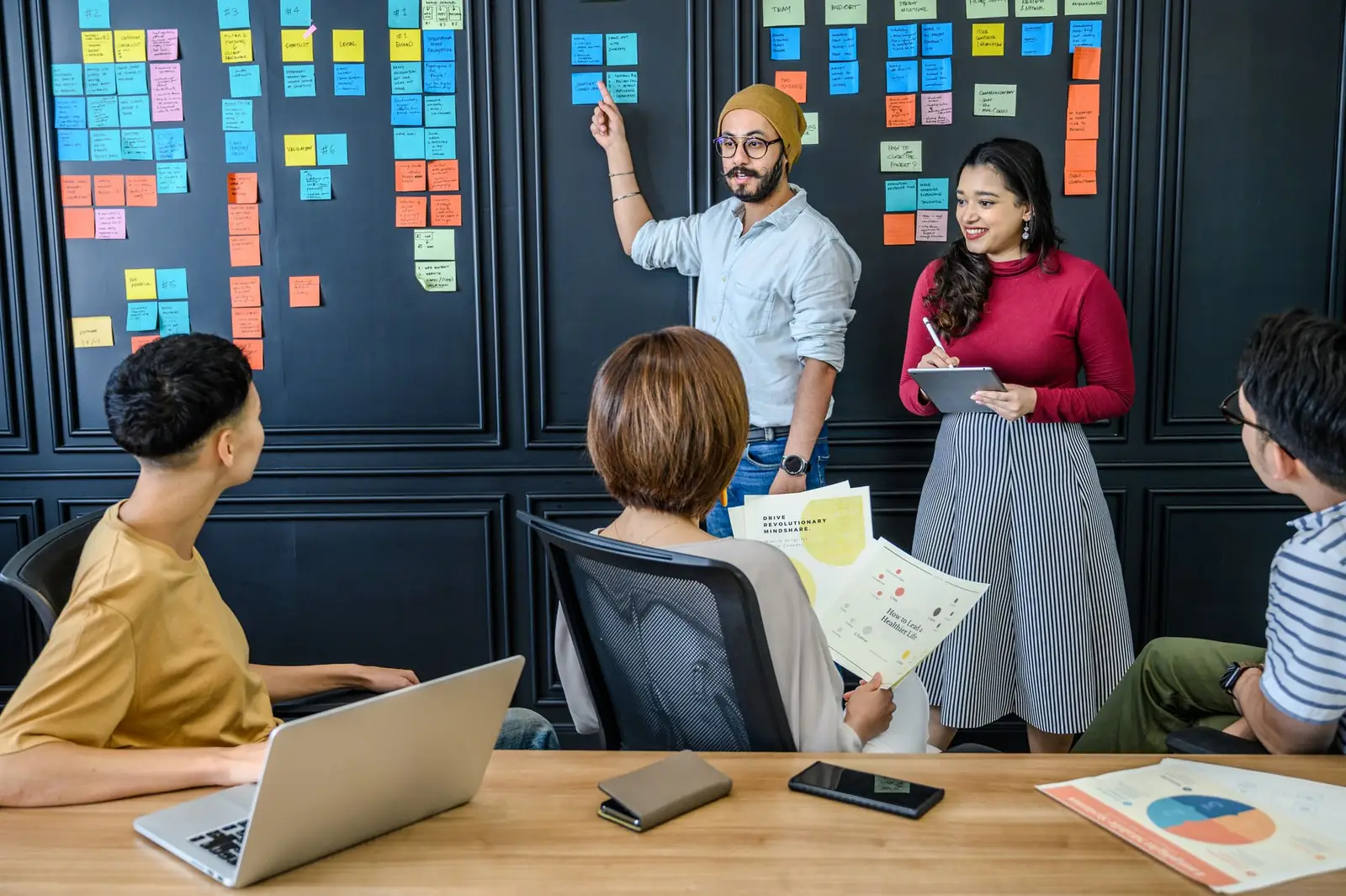 A strategist pointing at a sticky-note plan while a colleague takes notes